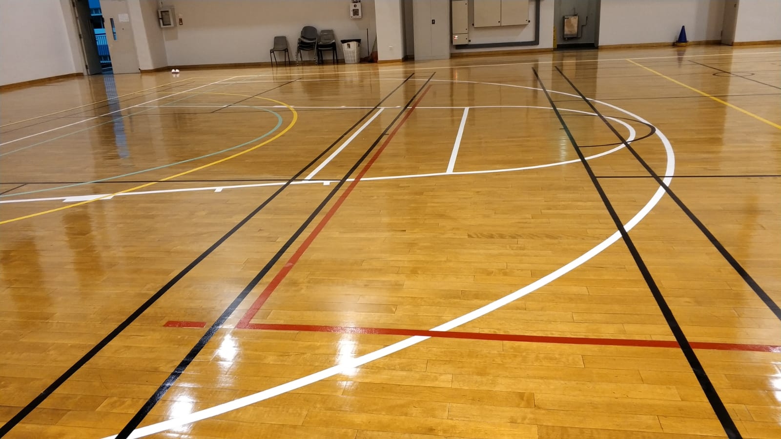 Multi-game court line marking on the timber sports floor at St Margaret Secondary School multi-purpose hall, showing basketball key, three-point arc and overlay lines