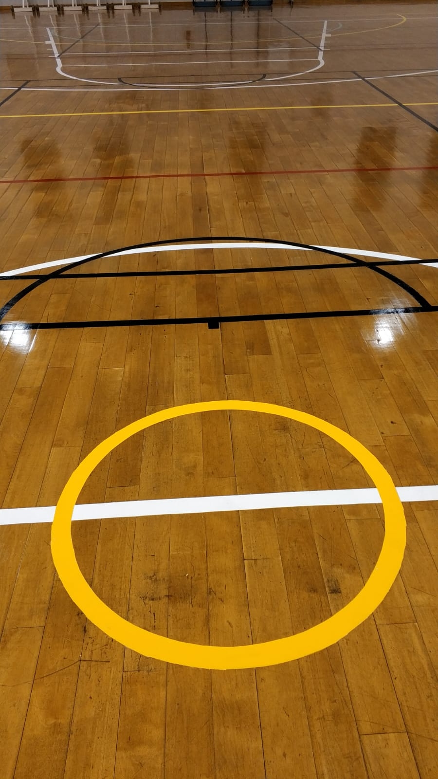 Freshly painted yellow centre circle and basketball key area on the timber floor at St Margaret Secondary School
